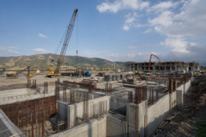 large construction site with heavy machinery, concrete structures, and mountain background, indicating construction holiday hiring needs.